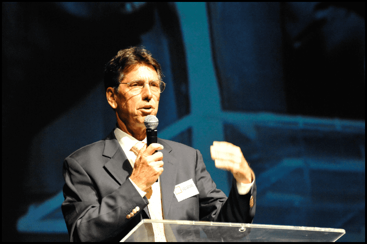 A photo of Warren Mosler speaking in front of an audience.